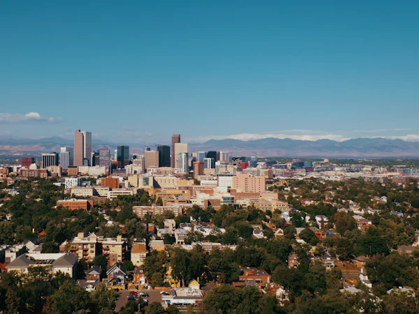 Downtown Denver above tree-lined neighbourhoods, with mountains on the horizon