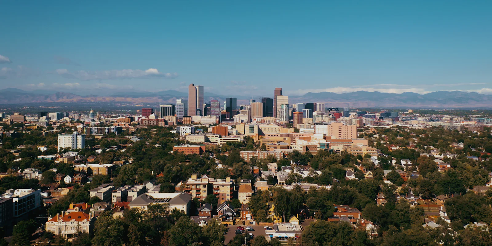Downtown Denver above tree-lined neighbourhoods, with mountains on the horizon