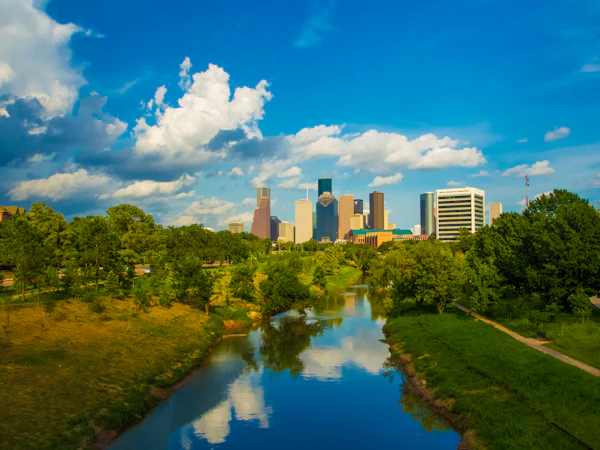 Downtown Houston seen along a tree-lined bayou under a blue sky