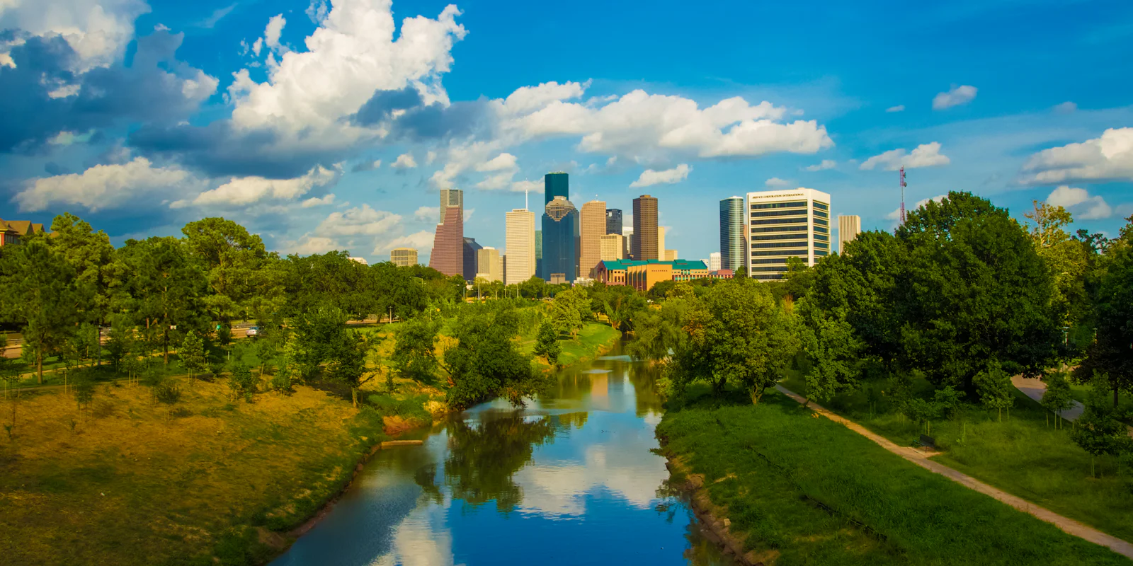 Downtown Houston seen along a tree-lined bayou under a blue sky