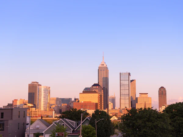 The Indianapolis skyline at dusk above trees and rooftops