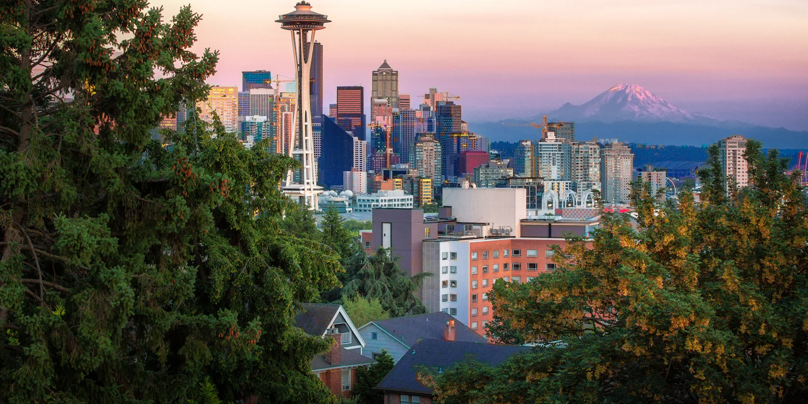 The Space Needle and downtown Seattle framed by trees, with Mount Rainier behind