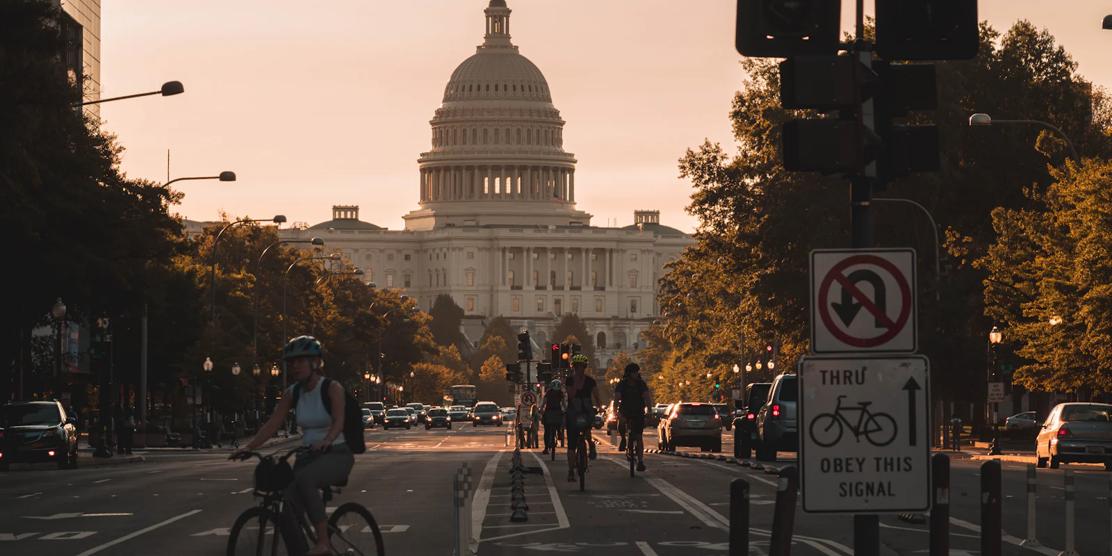 The US Capitol at the end of a street, with cyclists and traffic in warm evening light