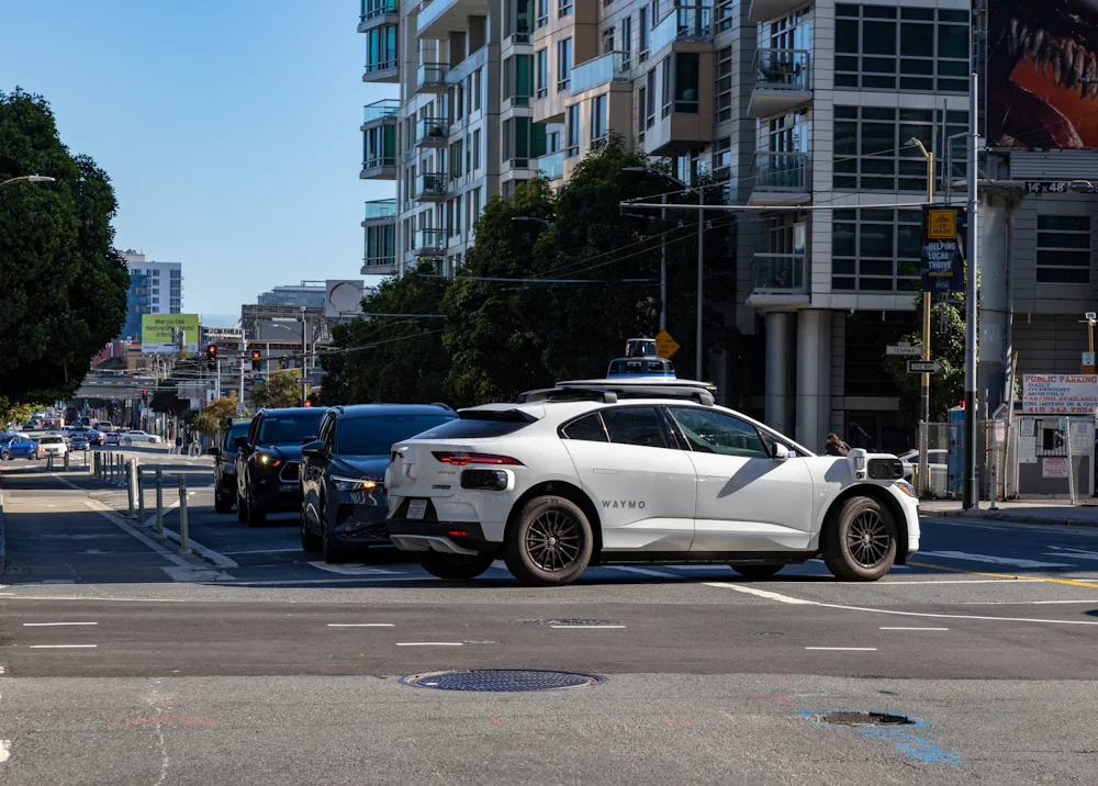 A white Waymo robotaxi stopped at a city intersection